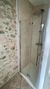 a glass shower in a bathroom with a stone wall at La Belle Histoire in Bize-Minervois