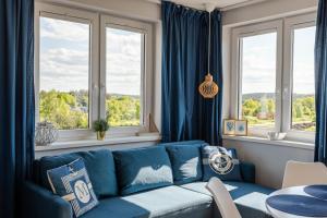 a blue couch in a living room with windows at Apartamenty Marynarskie 400m od plaży in Debina
