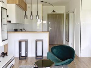 a living room with a green chair and a kitchen at Capital Towers - Apartament Modern w centrum miasta z widokiem na rzekę i park in Rzeszów
