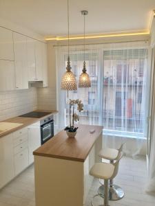 una cocina con armarios blancos y una isla con 2 sillas en Cloé Apartman, en Szeged