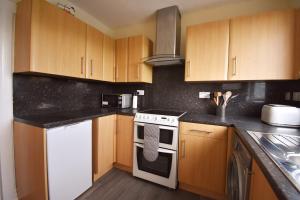 a kitchen with wooden cabinets and a white stove top oven at Jovie Apartment in Stornoway