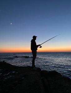 a man standing on a rock fishing on the ocean at Marina Golf Appart Chez Hicham in Asilah