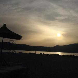 a sunset on a beach with a umbrella and water at Kompleksi Turistik EDIR in Orikum