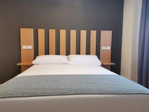 - un lit avec une tête de lit en bois et des oreillers blancs dans l'établissement Smart Hotel La Sagra, à Yuncos