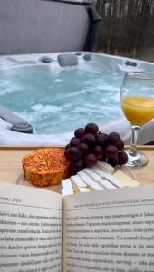 a book with a glass of wine and grapes next to a hot tub at Rubikiai LUX Duplex Apartamentai in Anykščiai