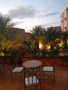 eine Terrasse mit einem Tisch, Stühlen und Palmen in der Unterkunft Riad Bouchedor in Ouarzazate