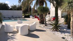een patio met witte stoelen en een zwembad met palmbomen bij Villa VINNER 1 Wellness & SPA in Monopoli
