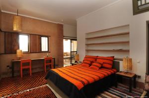 Schlafzimmer mit einem Bett mit orangefarbenen Kissen und einem Schreibtisch in der Unterkunft Dar al Hossoun in Taroudant