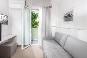 a white bedroom with a couch and a mirror at Hotel Centrale in Lignano Sabbiadoro