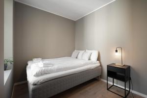 um pequeno quarto com uma cama com lençóis brancos e um candeeiro em Stay Nygård - Serviced apartments in central Bergen em Bergen