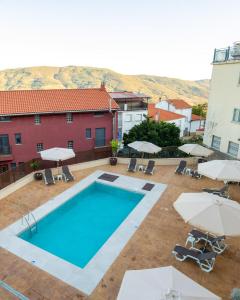 a swimming pool with umbrellas and chairs and a building at Natural&Mente Apartamentos Valle del Jerte in El Torno