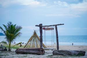 eine Schaukel am Strand mit einer Palme und dem Meer in der Unterkunft Holiday Villa Beach Resort Cherating in Cherating