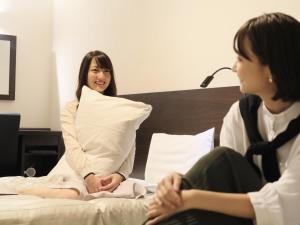 Eine Frau, die auf einem Bett sitzt und mit einer anderen Frau redet. in der Unterkunft Atsugi Urban Hotel in Atsugi