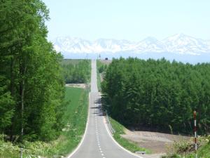 an empty road with snow covered mountains in the background at 旭川貸切一軒家プラスティ in Asahikawa