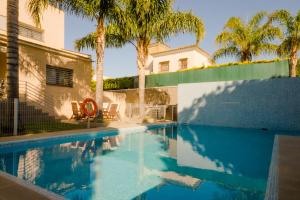 a swimming pool with two chairs and palm trees at La Casa del Mar in Chiclana de la Frontera