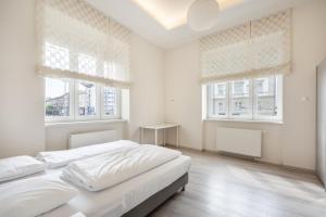 ein weißes Schlafzimmer mit einem Bett und zwei Fenstern in der Unterkunft Cascade Corvin Apartment in Budapest