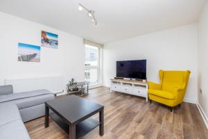 uma sala de estar com um sofá, uma televisão e uma cadeira amarela em ALTIDO Modern 2 bed flat near Inverleith Park, with terrace and free parking em Edimburgo