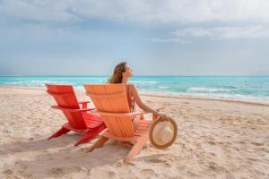 Al Alamein Hotel في العلمين: امرأة تجلس في مواجهة كرسيين للشاطئ على الشاطئ