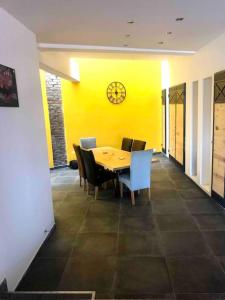 ein Esszimmer mit einem Tisch und einer Uhr an einer gelben Wand in der Unterkunft Loft atypique 192m2, terrasse, aux portes de Lille in Roubaix