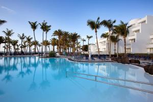 a large swimming pool with palm trees and buildings at Hipotels La Geria in Puerto del Carmen