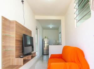 a living room with an orange chair and a flat screen tv at Casa com Piscina e Churrasqueira em Vera Cruz BA in Barra Grande