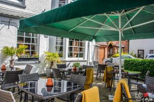 un patio con tavoli, sedie e un grande ombrellone verde di The Robin Hood Inn a Rowlands Castle