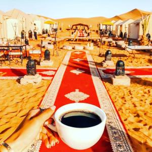 a person holding a cup of coffee in the desert at desert camp sahara luxury in Merzouga