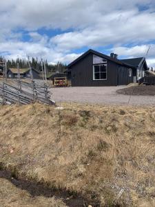 a black building with a fence next to a field at Beautiful cabin close to activities in Trysil, Trysilfjellet, with Sauna, 4 Bedrooms, 2 bathrooms and Wifi in Trysil