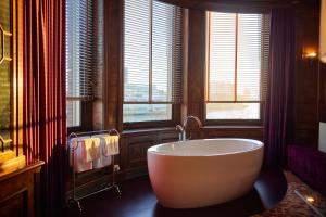 a bathroom with a tub in a room with windows at Hotel New York in Rotterdam