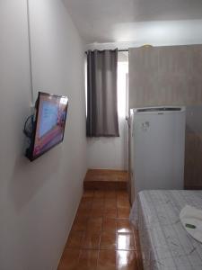 Habitación con TV en la pared y nevera. en Pousada bandeirantes en Ilhéus