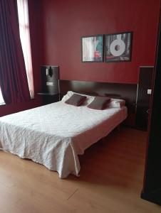 a bedroom with a bed with white sheets and red walls at Hotel / Restaurante LA PEPA in Avilés