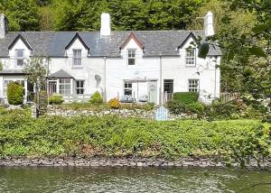 a white house with a river in front of it at Coorie Doon in Cairnbaan