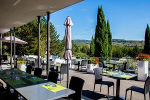 un patio con mesas, sillas y una sombrilla en Hôtel du cros d'Auzon en Saint-Maurice-dʼArdèche