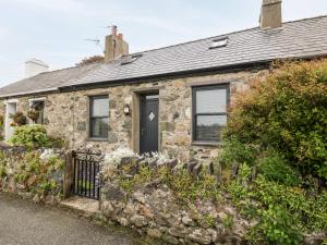 uma antiga casa de pedra com uma porta preta e janelas em 2 Rhoslyn em Caernarfon