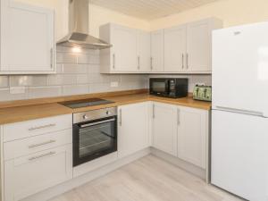 a white kitchen with white cabinets and a refrigerator at Arwelfa in Penmaen-mawr