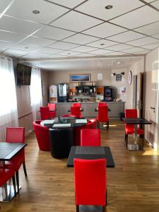 a dining room with red chairs and tables and a kitchen at L'Hôtel du Marais Romilly Centre in Romilly-sur-Seine