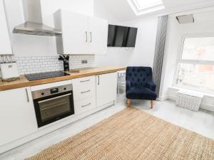 a kitchen with white cabinets and a blue chair at Sandpiper Apartment in Barmouth