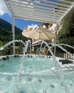 a swimming pool with an umbrella and a fountain at DU GLACIER Boutique & Traditions Hotel in Fiesch