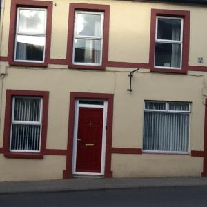 un edificio con una puerta roja y tres ventanas en Noreen Seans en Carndonagh