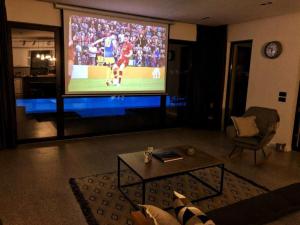 a living room with a large tv with a soccer game on it at Lake Breeze Villa with a Pool & Magnificent Views in Shirokë