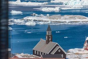 a church with icebergs in the water next to a building at Best Western Plus Hotel Ilulissat in Ilulissat