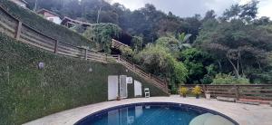 a swimming pool in front of a hill with a fence at Casa Itaipava Country Club in Petrópolis