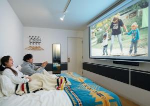 a group of people sitting on a bed watching a tv at Hotel Graphy Nezu in Tokyo