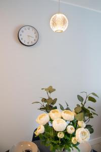 a vase with white flowers in a room with a clock at Maya's Flats & Resorts 52 - Aura 40 in Gdańsk