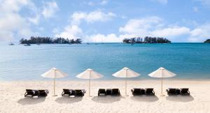a row of beach chairs with umbrellas on the beach at The Danna Langkawi Luxury Resort & Beach Villas in Pantai Kok