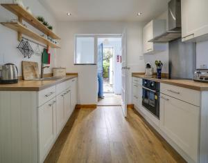 a kitchen with white cabinets and a wooden floor at Little Sark in Port Isaac