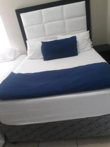 Una cama grande con una almohada azul. en Hotel Amor Rosebank en Johannesburgo
