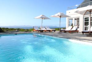 a swimming pool with chairs and umbrellas next to a house at 11 WESTCLIFF RENTALS in Hermanus