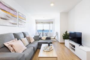 salon z szarą kanapą i telewizorem w obiekcie Home2Book Comfy Beachfront Radazul w mieście Radazul