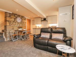a living room with a leather couch and a kitchen at Folly Cottage in Settle